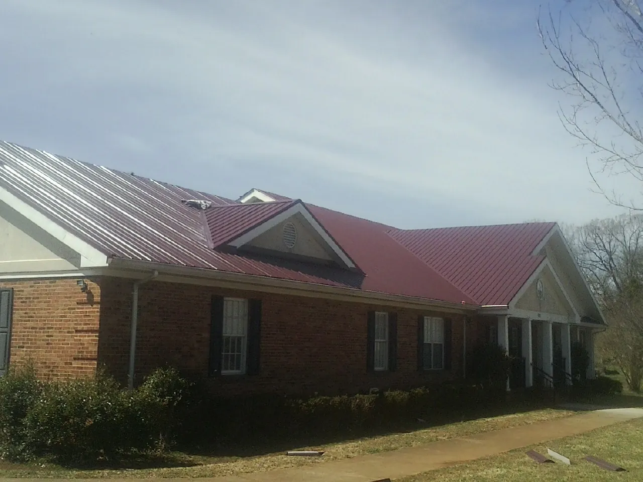 Red metal roof with gabled entries on a long brick building, from a Hail Damage Roof Repair job in Taylorville