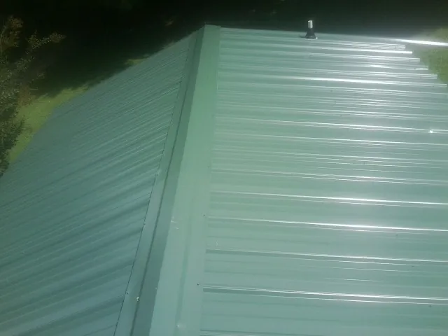 New green metal panels meeting at the ridge of a roof — Flat Roof Repair work by our crew in Taylorville