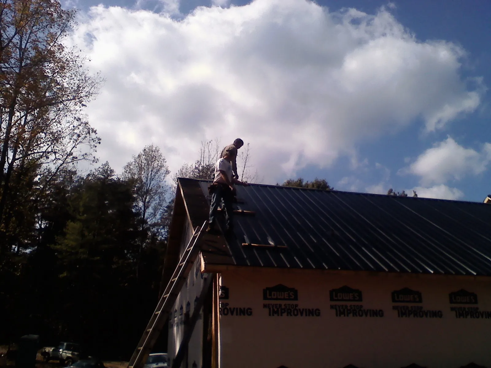 Roofer fastening dark metal panels high against a cloudy sky, from a Roof Inspection job in Taylorville