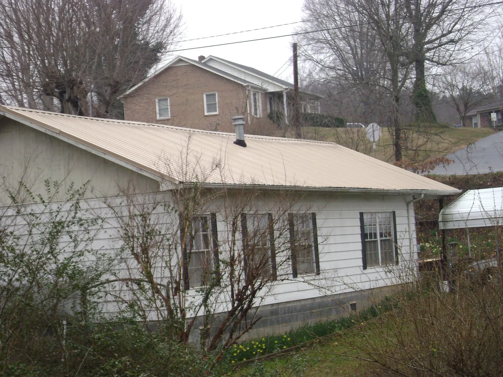 Tan metal roof on a white sided house set into a hillside — Commercial Roofing by Roofing Brothers in Taylorville