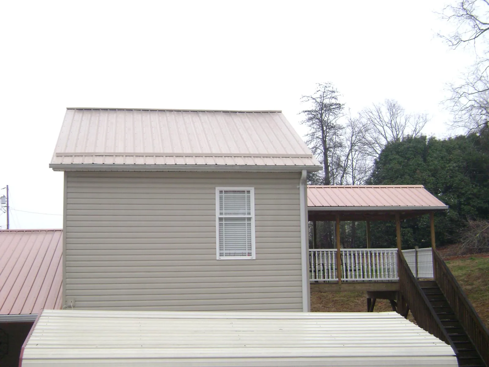 Tan metal roofs on a two story addition and attached porch, from a Roof Replacement job in Taylorville